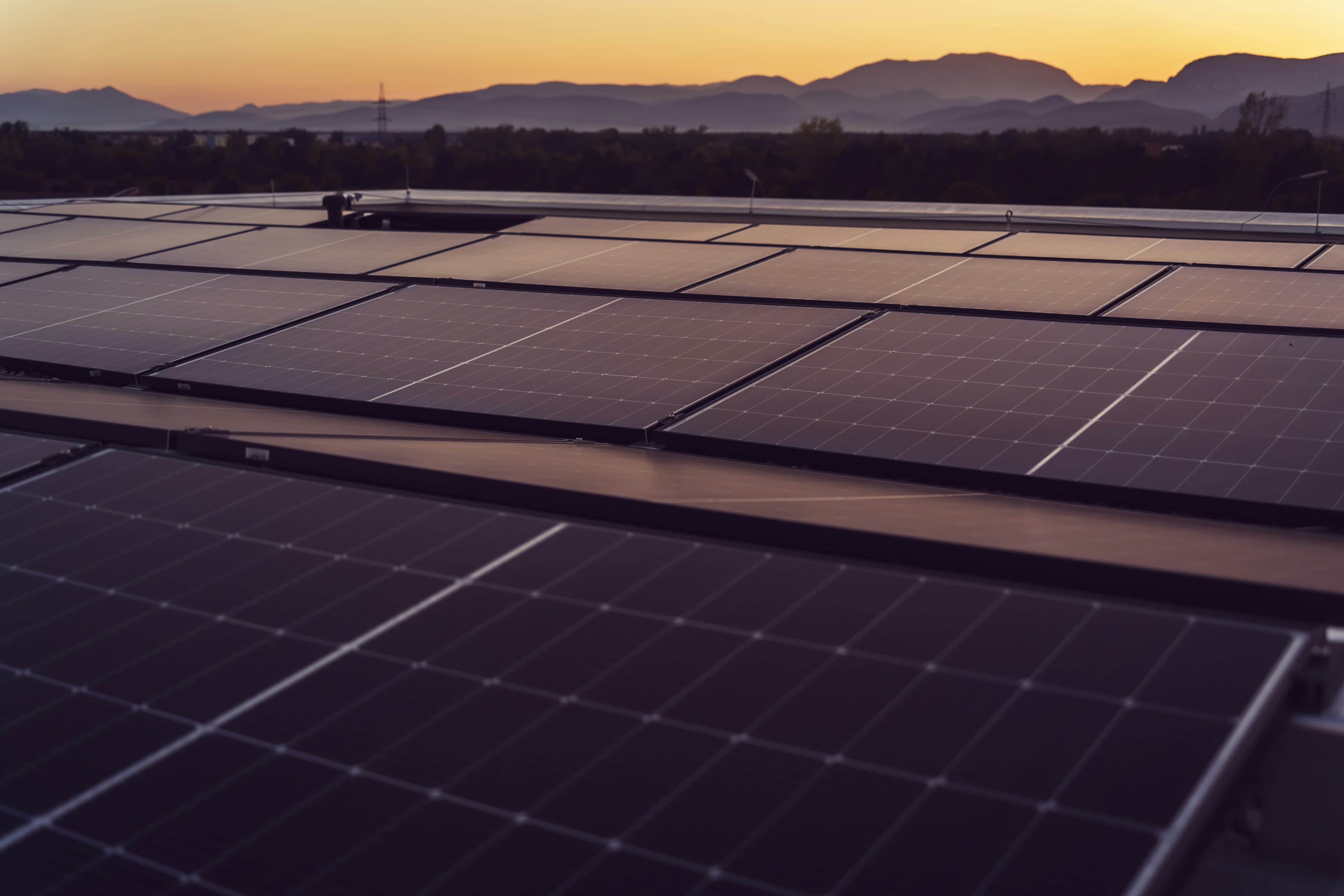 Photovoltaikanlage auf einem Flachdach vor Bergpanorama im Sonnenuntergang